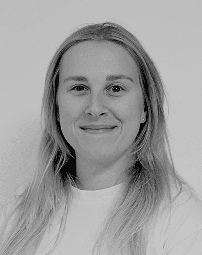 Et sort-hvidt portræt af en kvinde med langt, glat hår, iført en lys bluse, der smiler blidt til kameraet foran en ensfarvet baggrund.