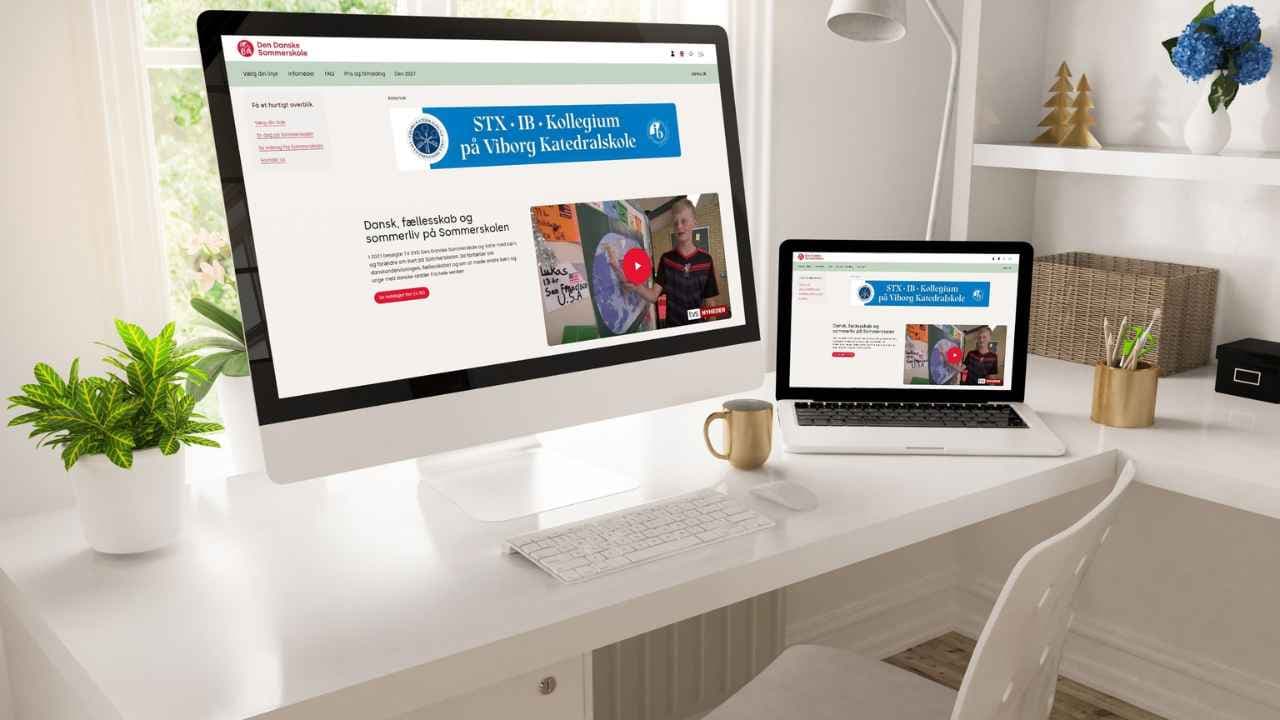 En stationær computer og en bærbar computer på et hvidt skrivebord, hvor begge viser den samme hjemmeside for STX-IB-Kollegium ved Viborg Katedralskole.