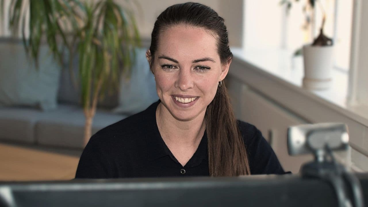 En smilende jurist sidder ved et skrivebord foran en computerskærm.